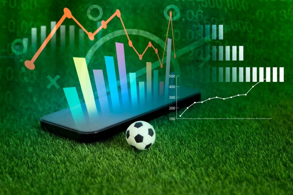 telefon cu statistici si o minge de fotbal pe gazonul unui teren